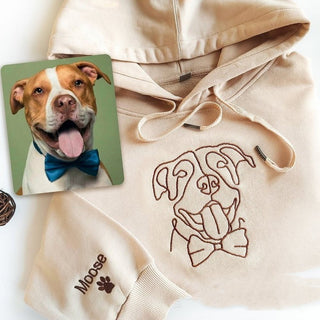 Playful dog with bowtie in image next to embroidered beige hoodie displaying dog graphic