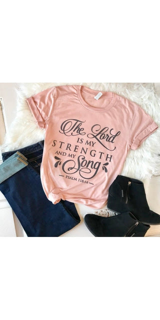 Pink women's fashion T-shirt with "The Lord is my strength and my song" slogan graphic, laid on a white background with a furry blanket or rug.