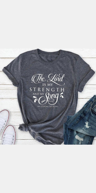 Stylish women's faith-inspired graphic tee with inspiring text "The Lord is my strength and song" in a vintage design on a charcoal gray background.