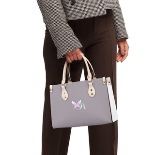 Stylish women's leather handbag with butterfly logo, held by a fashionably dressed person in a houndstooth coat and trousers.