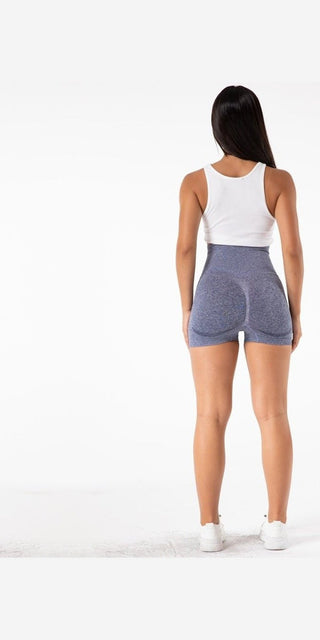 Relaxed fit yoga shorts in stylish grey color, modeled by a woman with long dark hair facing away from the camera on a plain white background.