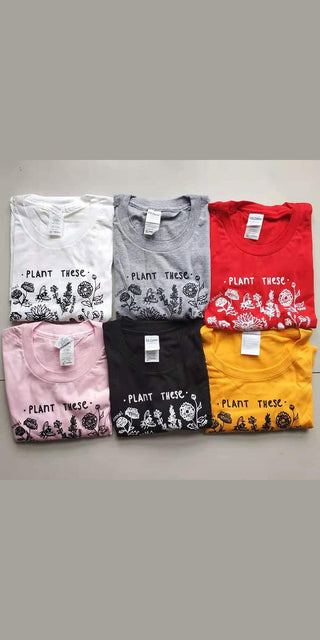 Vibrant plant-themed t-shirts in various colors and designs, featuring the text "Plant These" against a nature-inspired backdrop, showcasing a collection of trendy, eco-conscious women's apparel.
