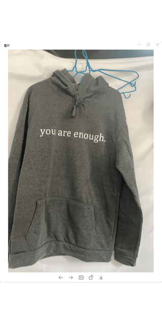 Cozy gray hoodie with inspirational message "you are enough" printed on the front, displayed on a hanger against a clean white background.