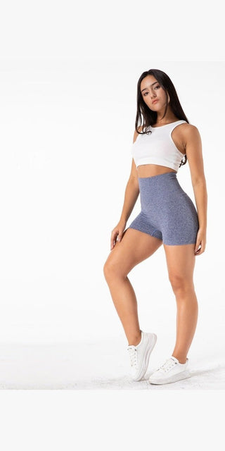 Sleek athletic woman in comfortable grey shorts and white crop top, posing confidently against a plain background.