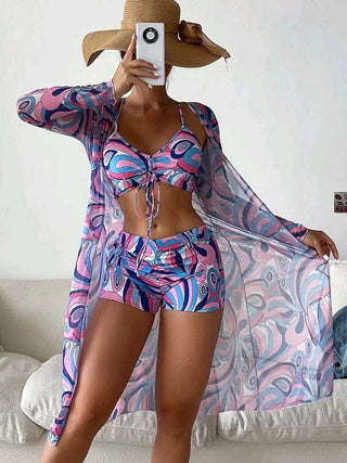Fashionable women's summer swimsuit with long sleeve cardigan. Bikini top features vibrant abstract print design. Coordinating shorts and lightweight cover-up create a stylish beach-ready ensemble.
