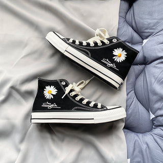 Stylish black and white high-top canvas sneakers with daisy flower design, resting on a gray fabric background.