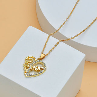 Sparkling heart-shaped pendant with "MOM" lettering and diamond accents on a delicate gold necklace, displayed on a minimalist white backdrop.