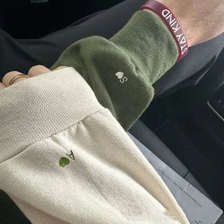 Cozy olive green fleece jacket with matching embroidered wristband, worn with beige knitted sweater against a dark background.