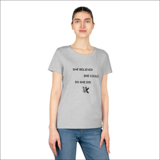 This image shows a woman wearing a gray t-shirt with text printed on it. The text reads "SHE BELIEVED SHE COULD SO SHE DID" along with a small design element. The woman in the image has a neutral facial expression and her hair is tied back. The background is plain and white.