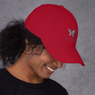 Red K-AROLE branded dad hat with butterfly logo on an smiling young woman with dark curly hair against a gray background.