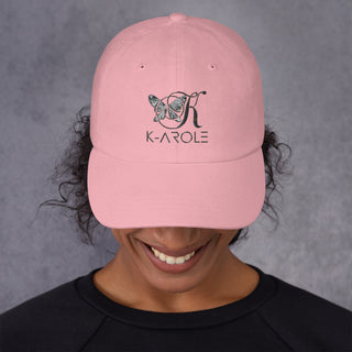 Fashionable pink dad hat with K-AROLE brand logo and butterfly design, worn by a smiling person