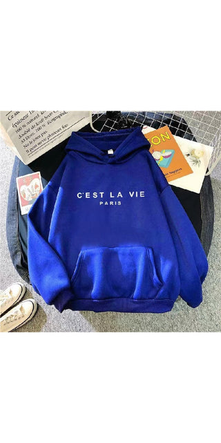 Blue hooded sweatshirt with "C'est la vie Paris" text print on the front, showcased on a light-colored background with other accessories.
