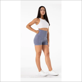 Stylish woman wearing white crop top and gray yoga shorts, posing confidently in the image.