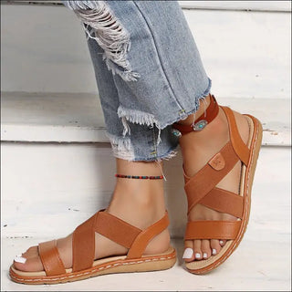 Strappy leather sandals with criss-cross design and neutral tone, worn with distressed denim jeans against a white background.