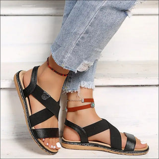 Stylish black and beige strappy women's sandals with a casual, comfortable design on display against a white wooden background.