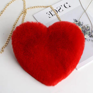 Plush Red Heart-Shaped Shoulder Bag - A vibrant, red, heart-shaped purse with a gold chain strap, resting on top of a fashion magazine against a white background.