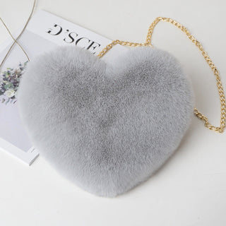 Plush gray heart-shaped purse with a gold chain strap showcased on a minimalist background with a fashion magazine.