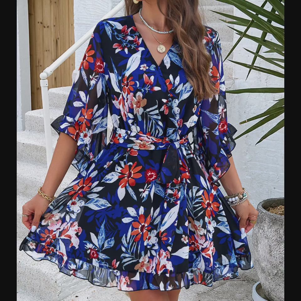 Vibrant floral print dress with frilled details and V-neck design, showcased on a female model in an outdoor setting with greenery.