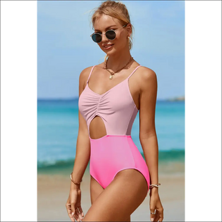 Stylish pink and neon pink cutout spaghetti strap one-piece swimwear, model posing on sandy beach with clear blue ocean in background.