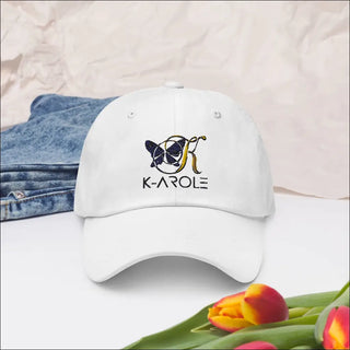 White stylish dad cap with the K-AROLE logo embroidered on the front, placed in a fashionable setting with denim and tulips.