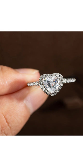 Elegant crystal heart-shaped wedding ring with sparkling diamond accents, showcased on a woman's hand against a dark background